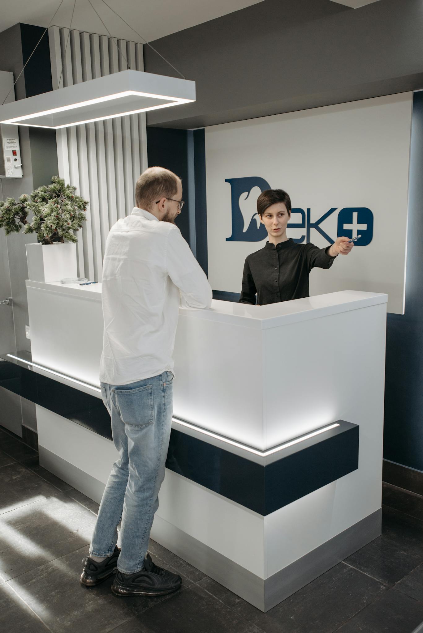Modern dental clinic reception area with a receptionist assisting a patient.
